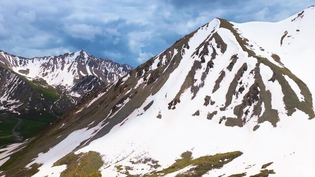 Snowy mountain peaks rise sharply against a cloudy sky along Duku Highway in Xinjiang, showcasing rugged terrain.