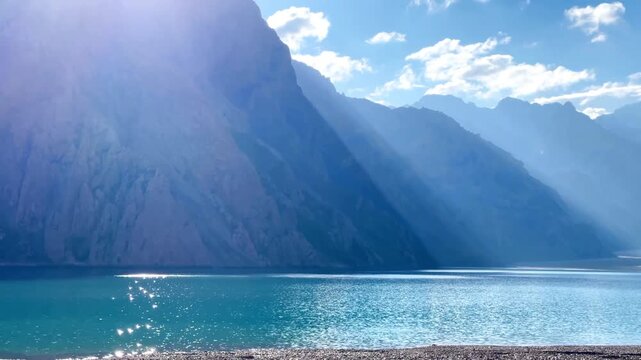 The front view of Tientang Hu Lake, Xinjiang, China. Many layers of mountains fill the background. The sun was rising, with sparkling reflections on the water. 