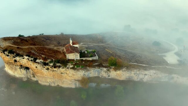 Peque&ntilde;a iglesia rom&aacute;nica de piedra construida sobre una colina rocosa con forma de barco al amanecer, con niebla en el Valle de Losa, Arquitectura medieval antigua, templo hist&oacute;rico rural, Pantale&oacute;n.