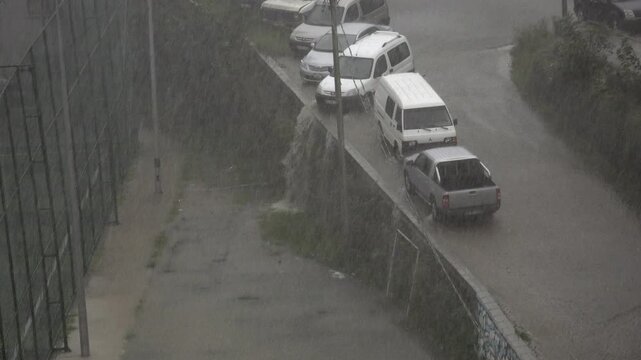 Extreme rain pounds a city street as overflowing water rushes along the road.
