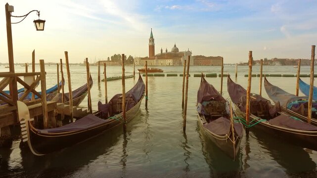 View of traditional gondolas moored at wooden poles in the Venetian lagoon with the San Giorgio Maggiore church in the background, Venice, Veneto, Italy.