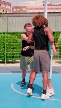 vertical Young multicultural friends playing intense streetball game outdoors