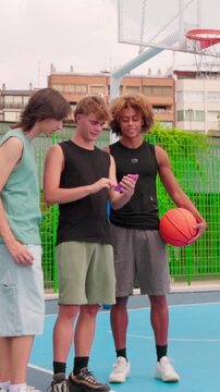 vertical Multicultural friends laughing together using smartphone on basketball court
