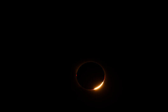 Total solar eclipse showing the bright diamond ring effect as sunlight emerges from behind the Moon. The last intense arc of the solar photosphere illuminates the lunar silhouette, while red solar pro