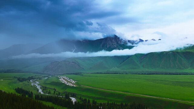 Dramatic clouds and mist envelope majestic mountains over lush green pastures along the scenic Duku Highway in Xinjiang.