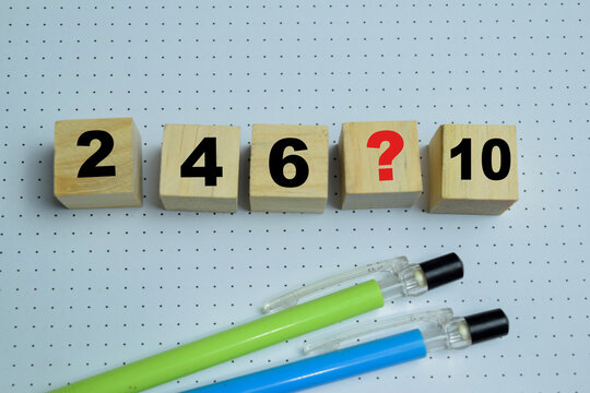 Missing number in mathematical sequence with number two, four, six, ten and question text stacked wooden cubes on the table