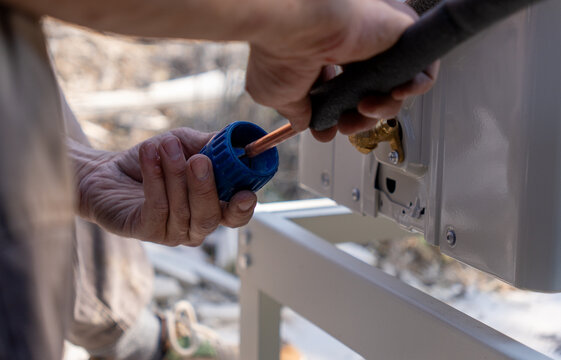  a technician installing an outdoor air conditioner unit, working with a copper pipe in insulation. Professional HVAC technician fitting or repairing a split system cooling equipment