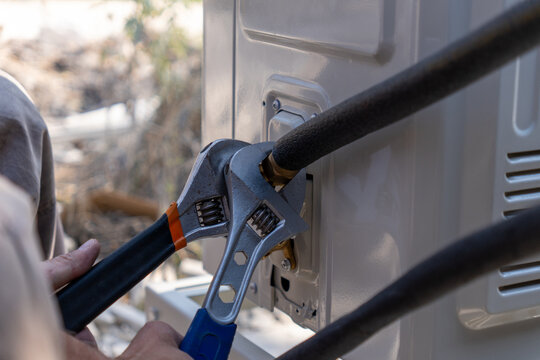 Close-up of a technician tightening a brass nut on a copper pipe with adjustable wrenches during air conditioner installation. Professional HVAC service, maintenance and split system connection