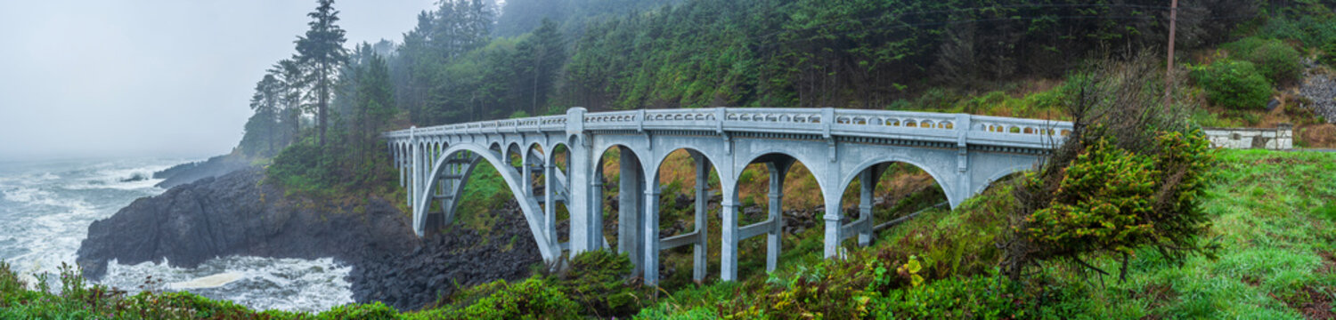 Beautiful wide panoramic view of an old arched concrete bridge on a misty rocky ocean coast