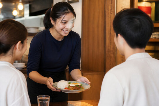 外国人ホールスタッフが日本人客に料理を提供する飲食店の接客風景