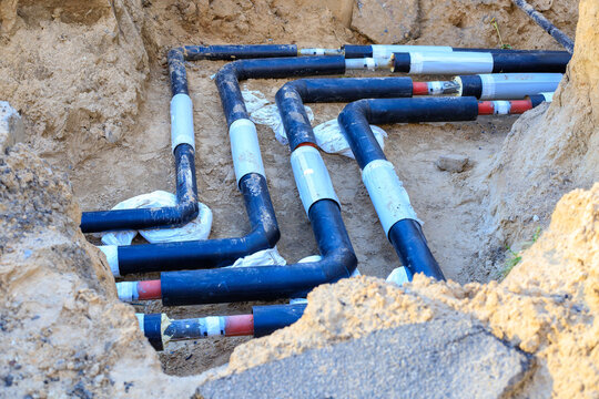 Excavated trench containing black pipes during outdoor replacement work