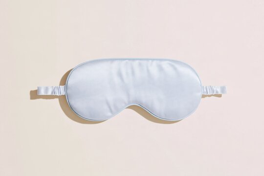 Sleep mask made of smooth satin, featuring a pale silver grey sheen on a neutral soft surface for bedtime and wellness accessories