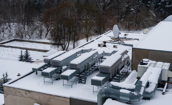 View of a snow-covered rooftop featuring multiple HVAC units, ventilation ducts, and a satellite dish in Vilnius, Vilnius County, Lithuania.