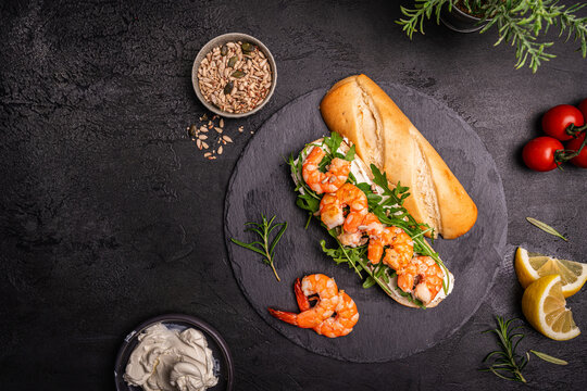 Healthy shrimp sandwiches for breakfast, snack, appetizers Toast with grilled prawns and whole grain bread with cream cheese and arugula on a dark background, top view