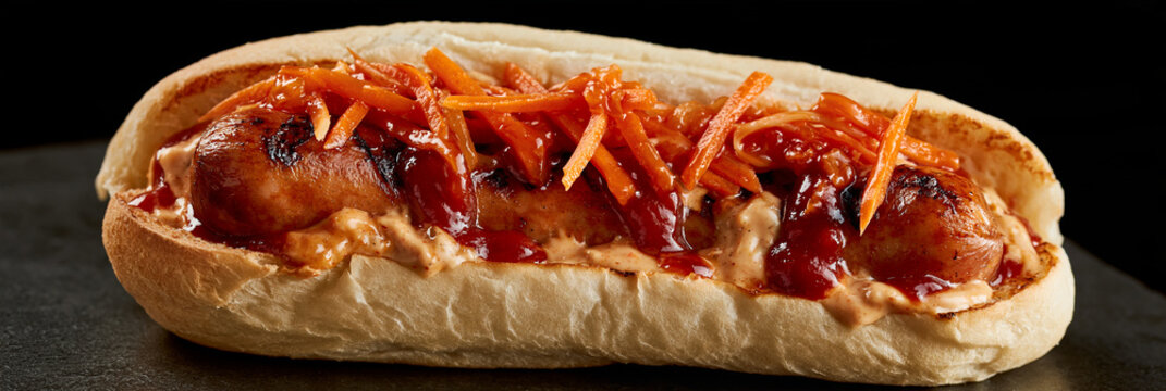 Hotdog mit Bratwurst, geriebenen Karotten und roter Sauce