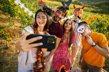 Obraz premium Group of cheerful friends taking a selfie at an outdoor Halloween party in a vineyard.