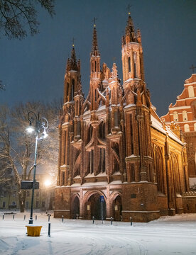 View of the illuminated Gothic facade of St. Anne's Church during a winter night with snow-covered ground in Vilnius, Vilnius County, Lithuania.