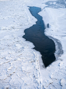 View of a frozen river with floating ice floes and a patch of open dark water in Vilnius, Vilnius County, Lithuania.