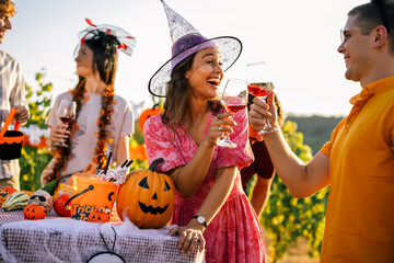 Obraz premium Woman in a witch hat clinking wine glasses with a friend at an outdoor Halloween party.