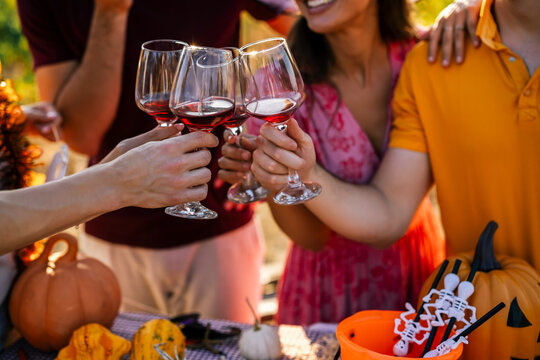 Detailed close-up of young people cheering with red wine glasses during an outdoor autumn Halloween party.
