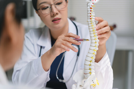 Doctor consulting patient, pointing at a spine model during an orthopedic examination. Healthcare and chiropractic concept