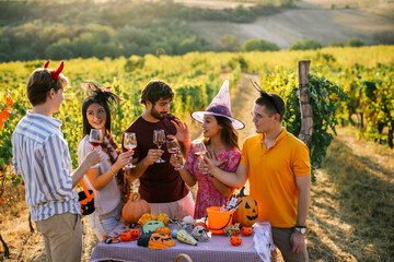 Obraz premium Group of friends in Halloween costumes standing around a decorated table and enjoying wine in a vineyard.