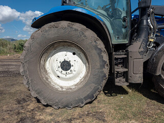 Close up of a modern blue farm tractor showing cabin and large muddy wheel © catocala