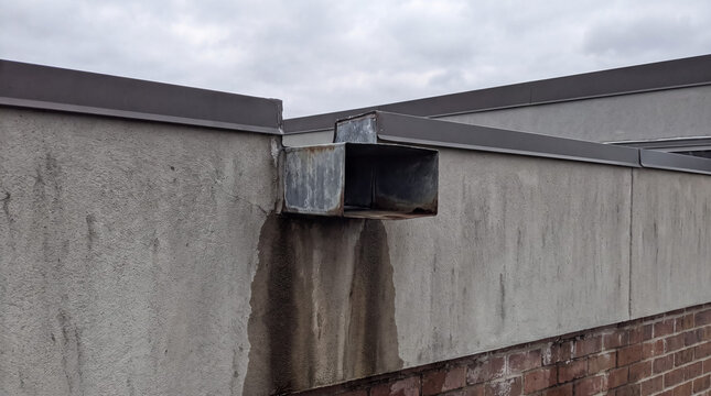 Building exterior with a metal scupper draining water, creating stains and demonstrating needed maintenance