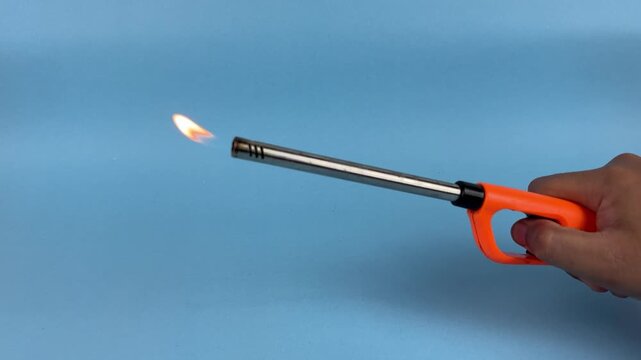 Hand Holding Long Gas Lighter with Flame on Blue Background