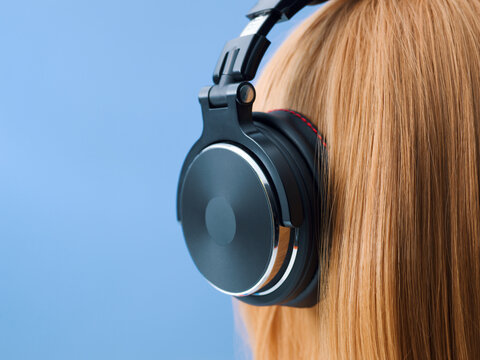 Close-up Side View of Redhead Girl Wearing Professional Black Headphones on Blue Background