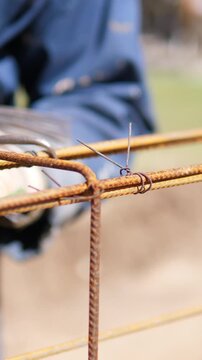 Gloved hands secure steel reinforcement with hand tool on outdoor building site, showing rusted metal grid, blurred workwear, warm natural light, and practical labor detail for industrial projects