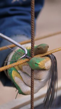 Close-up view of gloved hands twisting steel rebar and fastening wire in reinforced concrete grid, showing rusty texture, muted colors, and careful manual craftsmanship on indoor worksite