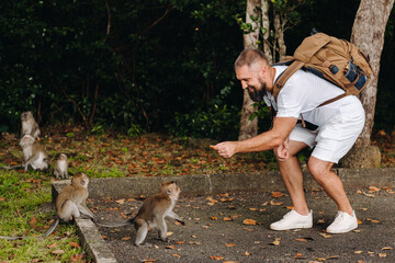 Mauritius island. a tourist with a backpack feeds monkeys by the side of the road in the jungle.A traveler in a white t shirt with a backpack plays with monkeys in Africa the island of Mauritius © Alex