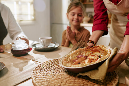 Senior Caucasian woman serving fresh baked apple pie to smiling Caucasian girl grandchild at dining table. Concept of family routine suitable for bakery or culinary advertising