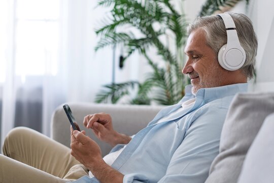 Smiling middle-aged man wearing headphones listen to mobile music playing in smartphone app