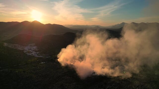 Aerial view of burning garbage dump pollution at sunset. Lot of smoke from the landfill near the city, environmental pollution. Drone shot of nature destruction
