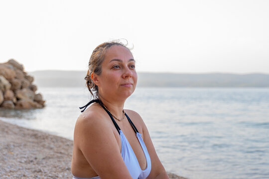 Thoughtful woman relaxing on a quiet pebble beach by sea