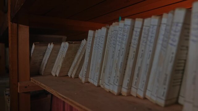 Old archive folders with radio reel recordings stand on wooden shelves in warm light. Concept of audio preservation, media history, library, research, heritage, broadcast archive.