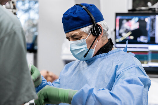 Cardiologist during catheter examination of the patient&rsquo;s coronary arteries in a cath lab with medical monitors and equipment.