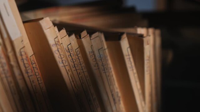 Old archive folders with radio reel recordings stand on wooden shelves in warm light. Concept of audio preservation, media history, library, research, heritage, broadcast archive.