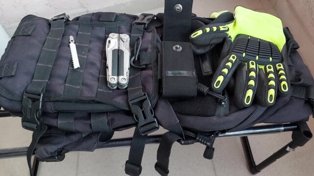 Folded heavy duty multitool lying on black tactical backpack background, top view close up with smooth zoom