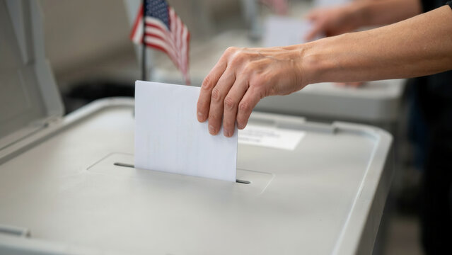 Close up of a person inserting a white paper ballot into a voting machine at a polling station