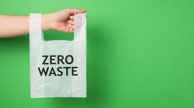 Hand holding a biodegradable plastic bag with Zero Waste text on a green background.