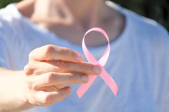 Middle aged woman hand holding pink ribbon toward camera. Breast cancer awareness month concept