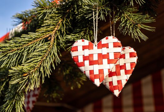 Woven red and white heart ornaments hanging on pine branch