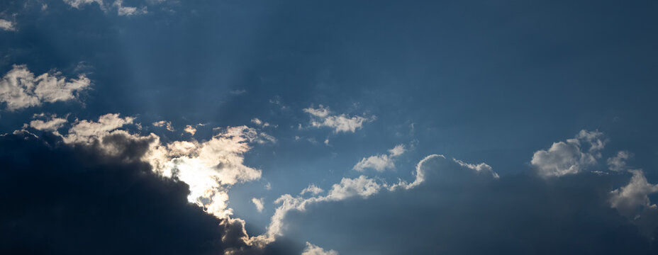 Sunbeams breaking through dark clouds in blue sky