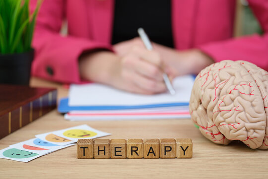 In a cozy therapy room, a therapist writes notes while colorful emotion cards and a model brain sit nearby. This scene reflects the importance of mental health awareness and communication.