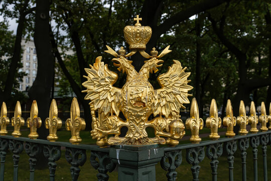 Ornate gilded double-headed eagle and golden finials on historic wrought iron fence in a Saint Petersburg park.
