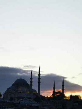 Silhouette of a large mosque with minarets against sunset sky. Dramatic evening lighting highlights Islamic architecture and city landscape.
