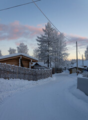 A winding snowy road, fences and private village houses in the Far North of Russia at pastel twilight. © PuzzleSoul